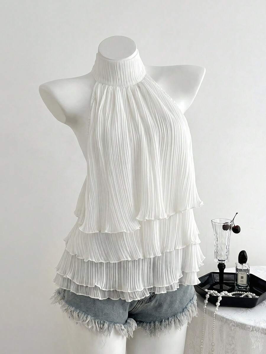 Women's white sleeveless halter neck top featuring pleated fabric, backless tie strap design, and a flared layered ruffle hem.