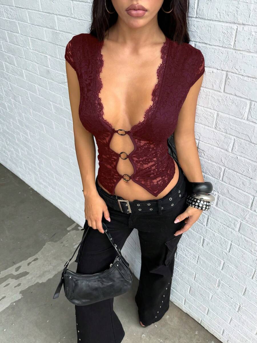 Women's black slim fit semi-sheer blouse featuring contrast lace detailing, a deep V hollow design with ring accent, asymmetrical hem, and cap sleeves.
