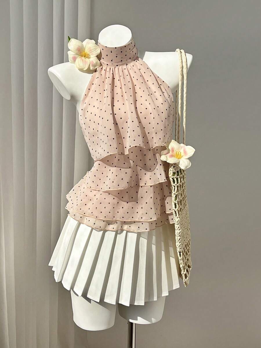 Women's white sleeveless halter neck top featuring pleated fabric, backless tie strap design, and a flared layered ruffle hem.