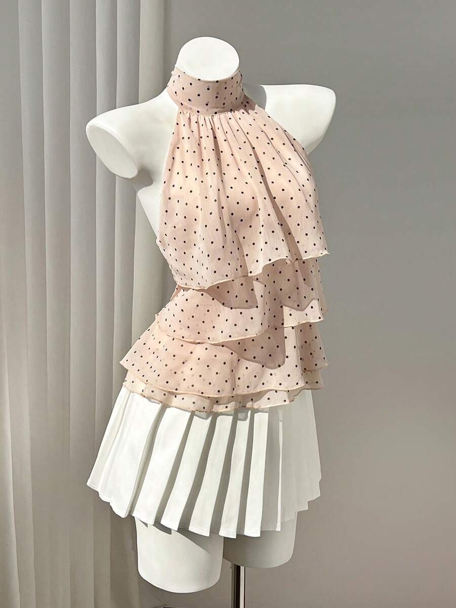 Women's white sleeveless halter neck top featuring pleated fabric, backless tie strap design, and a flared layered ruffle hem.