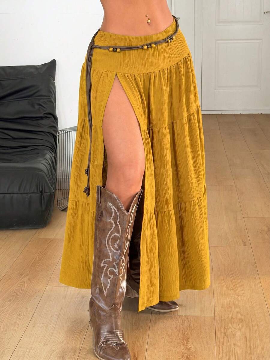 Mustard yellow low waist long skirt with a split thigh design and flared tiered hem in textured woven fabric for women.