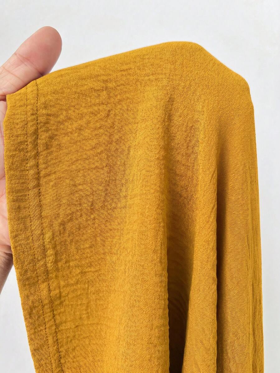 Mustard yellow low waist long skirt with a split thigh design and flared tiered hem in textured woven fabric for women.