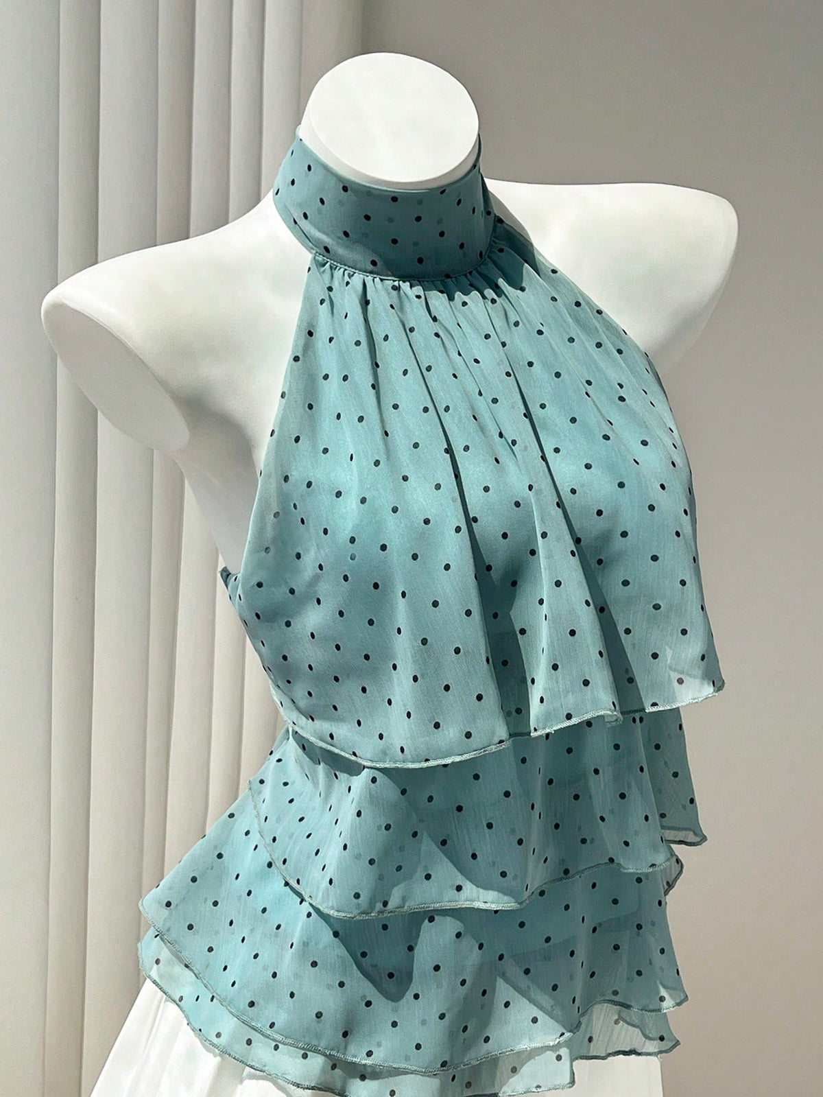 Women's white sleeveless halter neck top featuring pleated fabric, backless tie strap design, and a flared layered ruffle hem.