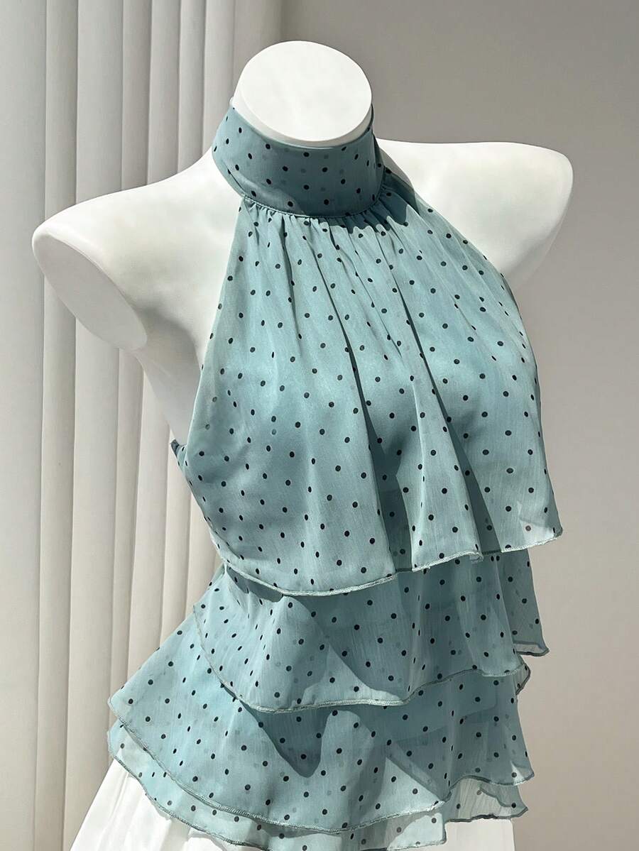 Women's white sleeveless halter neck top featuring pleated fabric, backless tie strap design, and a flared layered ruffle hem.
