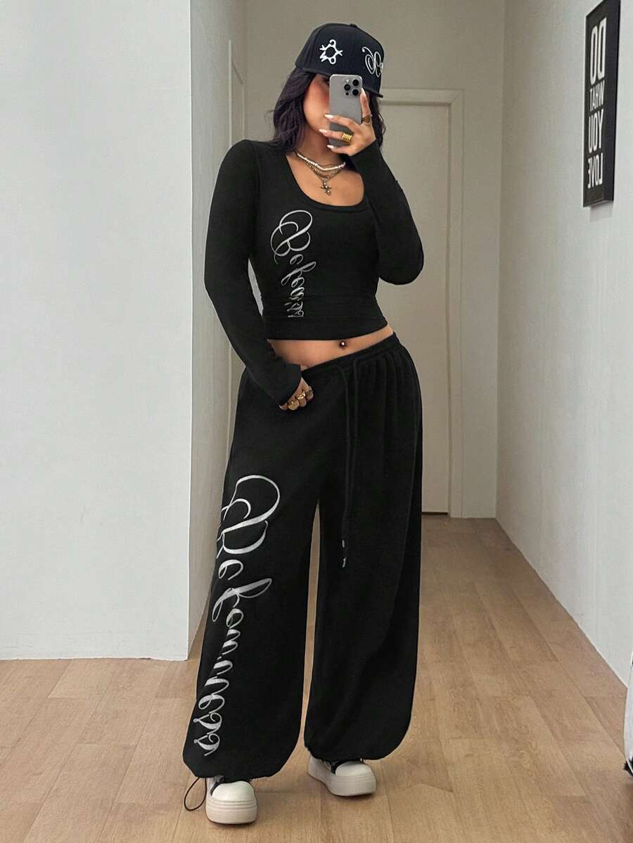 Women's black two-piece casual outfit featuring a long sleeve scoop neck letter print t-shirt and matching wide leg sweatpants made of knitted cotton blend fabric.