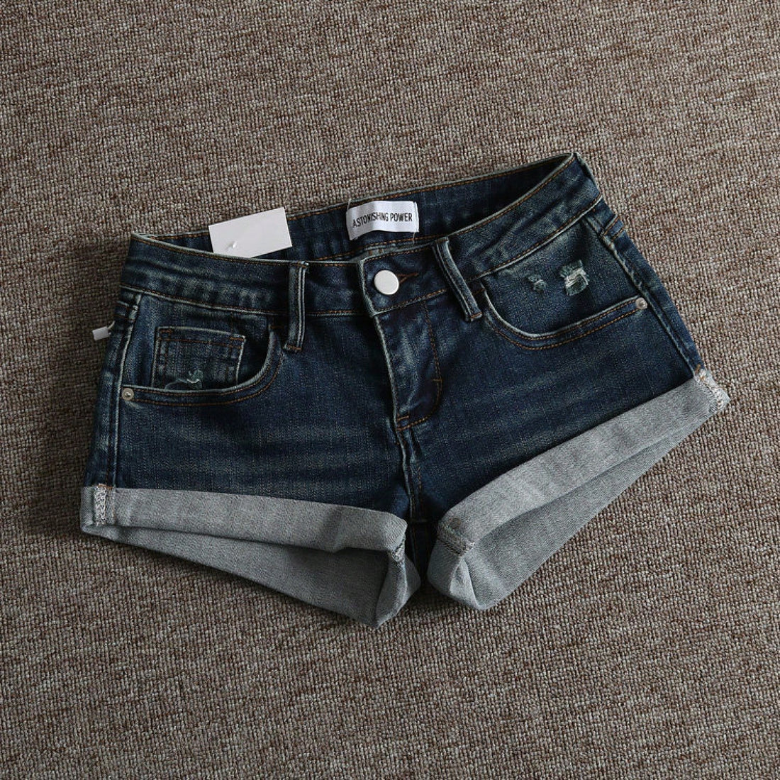 Women's low-waist shorts with ripped hem, asymmetrical detail, straight-leg cut, and pockets.