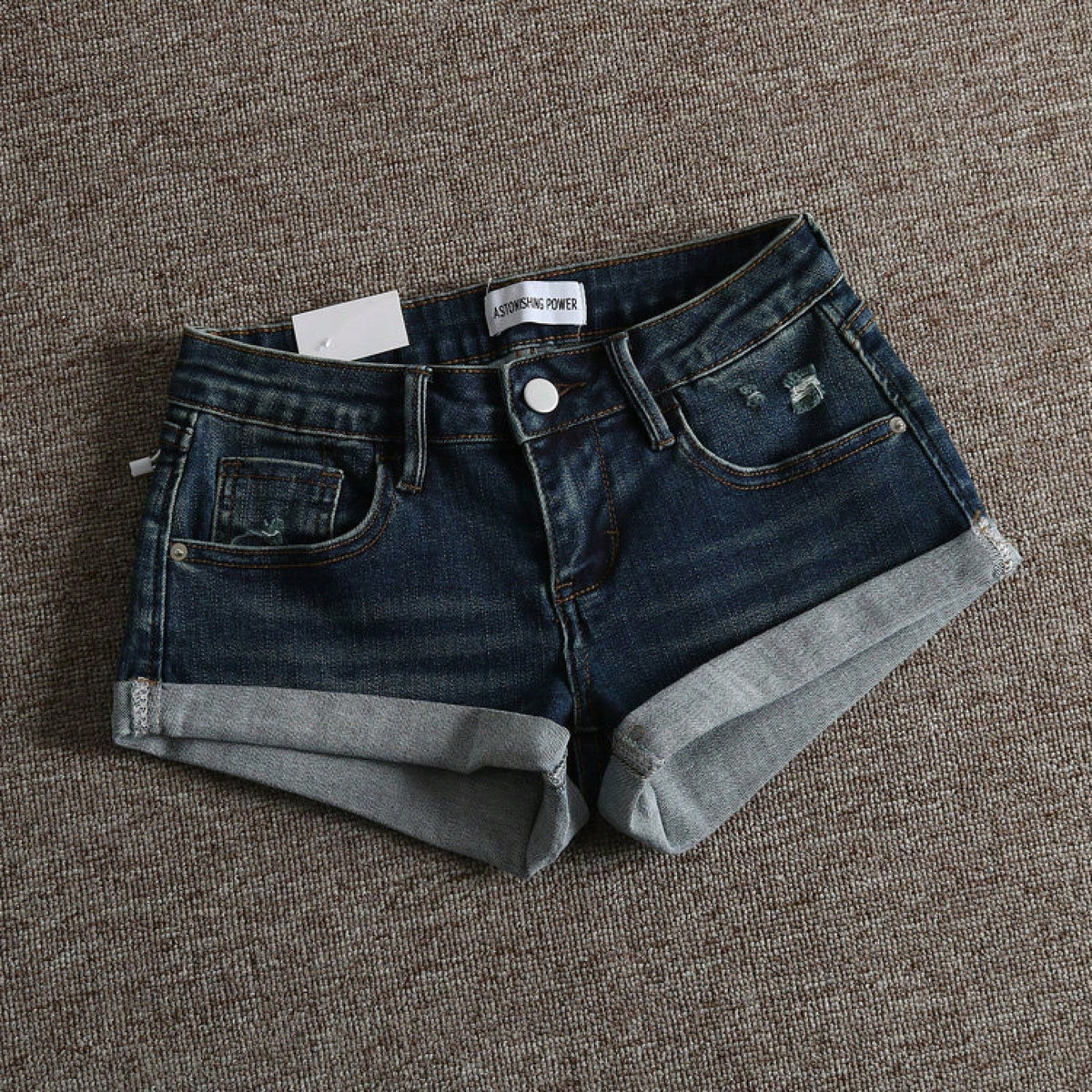 Women's low-waist shorts with ripped hem, asymmetrical detail, straight-leg cut, and pockets.