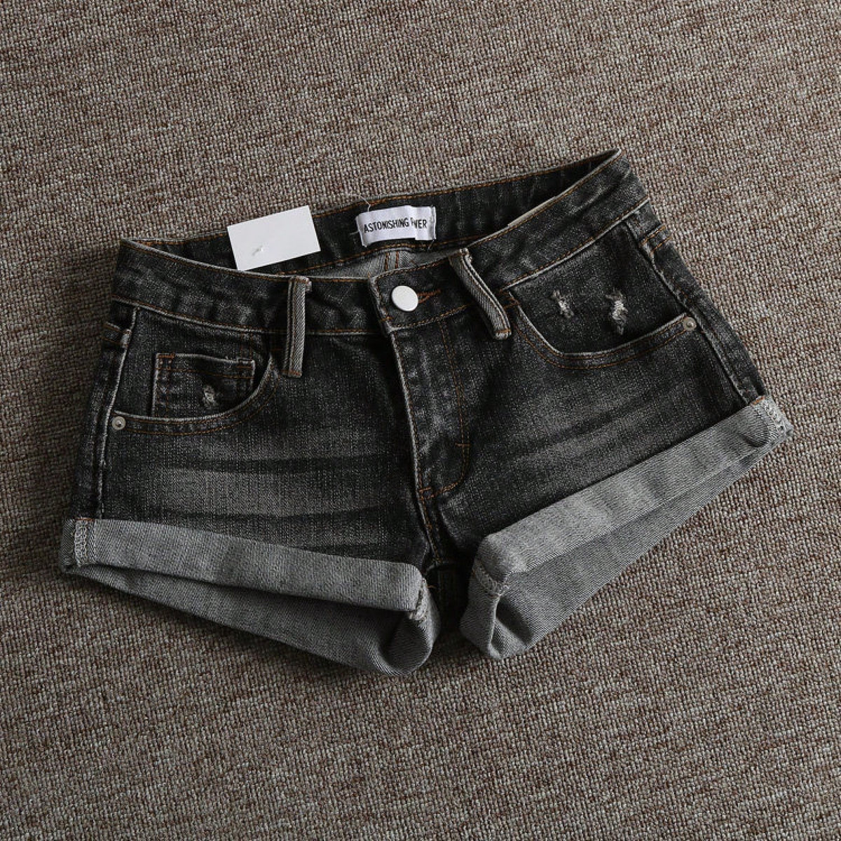 Women's low-waist shorts with ripped hem, asymmetrical detail, straight-leg cut, and pockets.