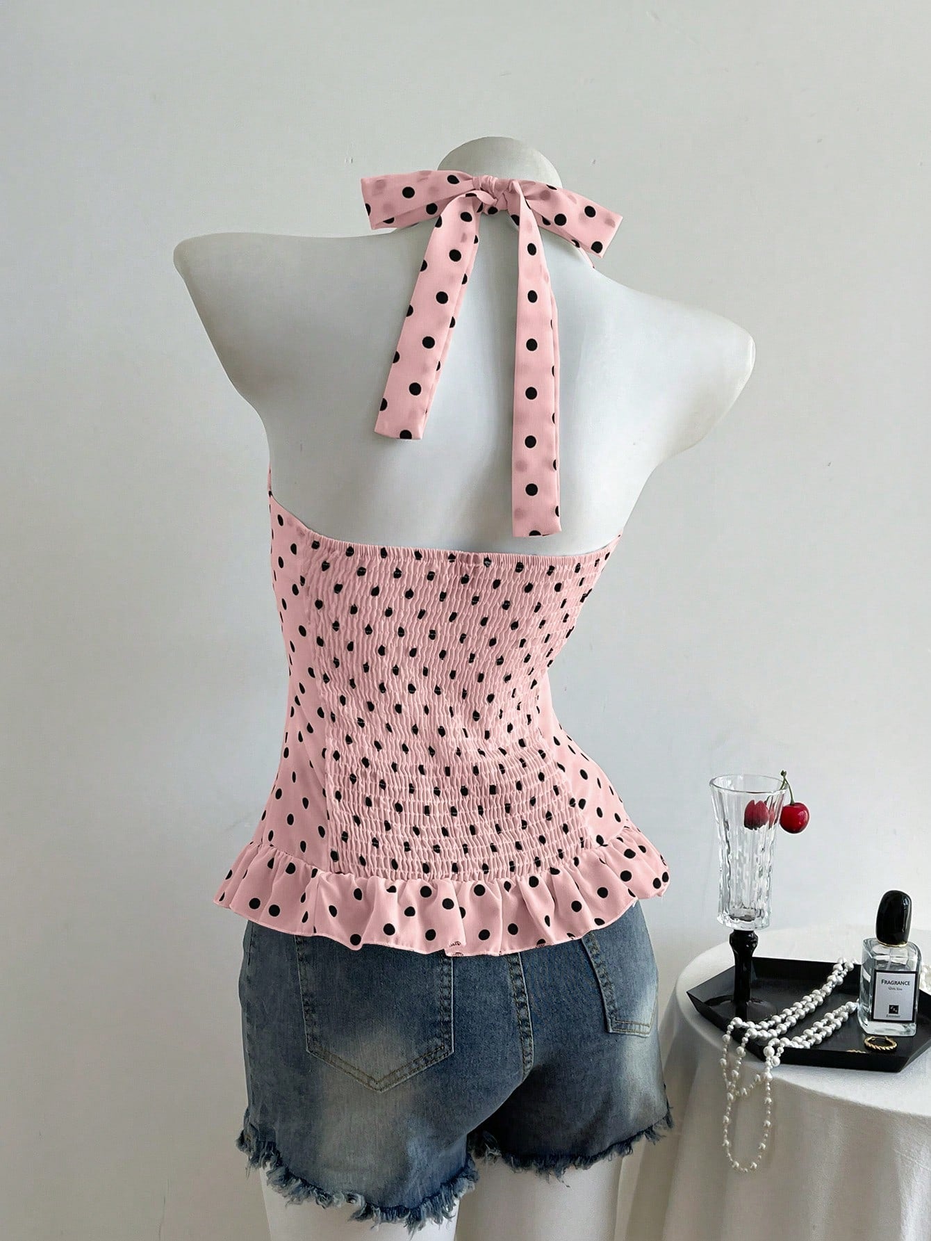 Women's polka dot halter camisole with bow bust detail, ruched and shirred design, slim crop fit, and flared ruffle hem.