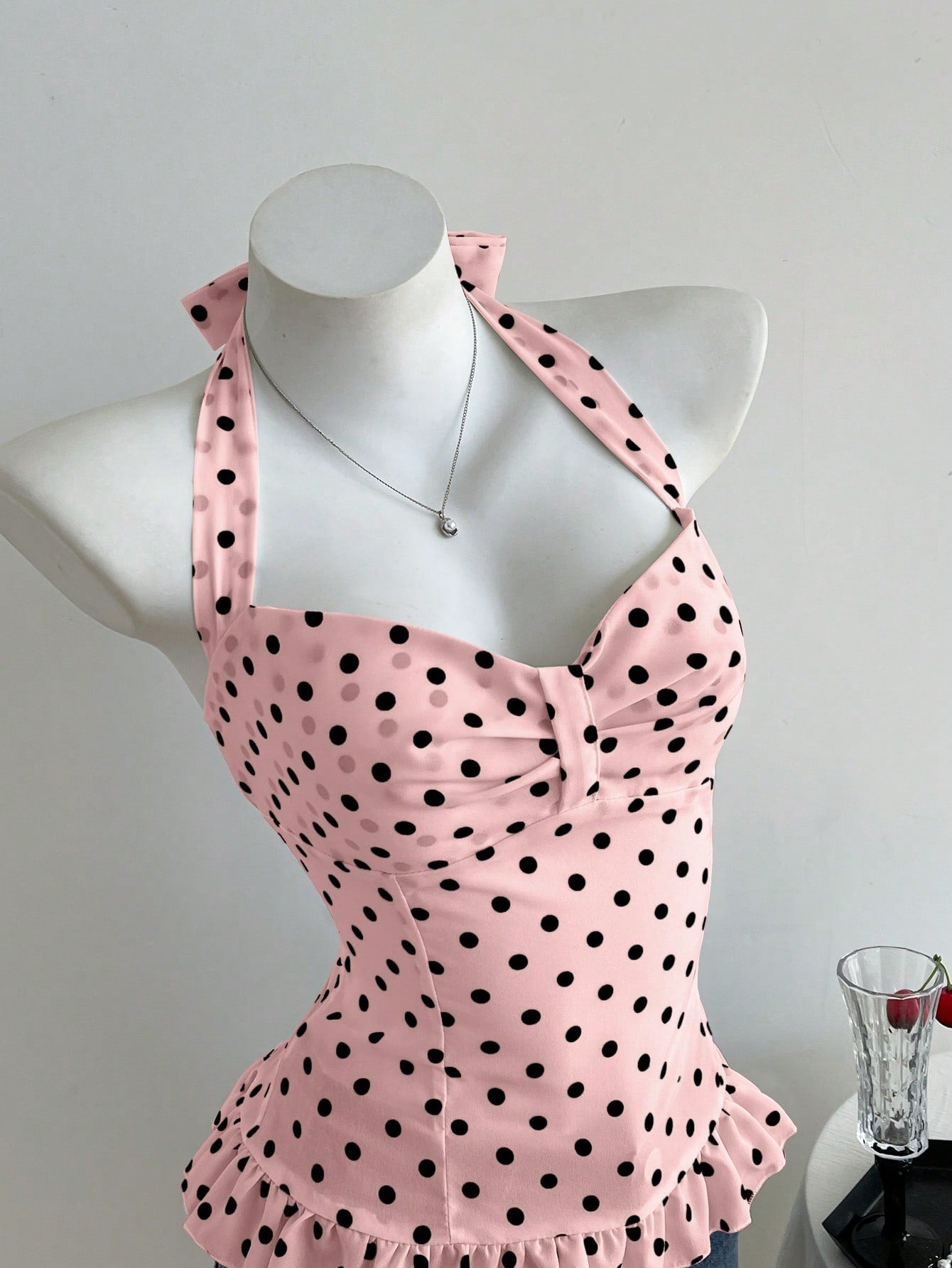 Women's polka dot halter camisole with bow bust detail, ruched and shirred design, slim crop fit, and flared ruffle hem.