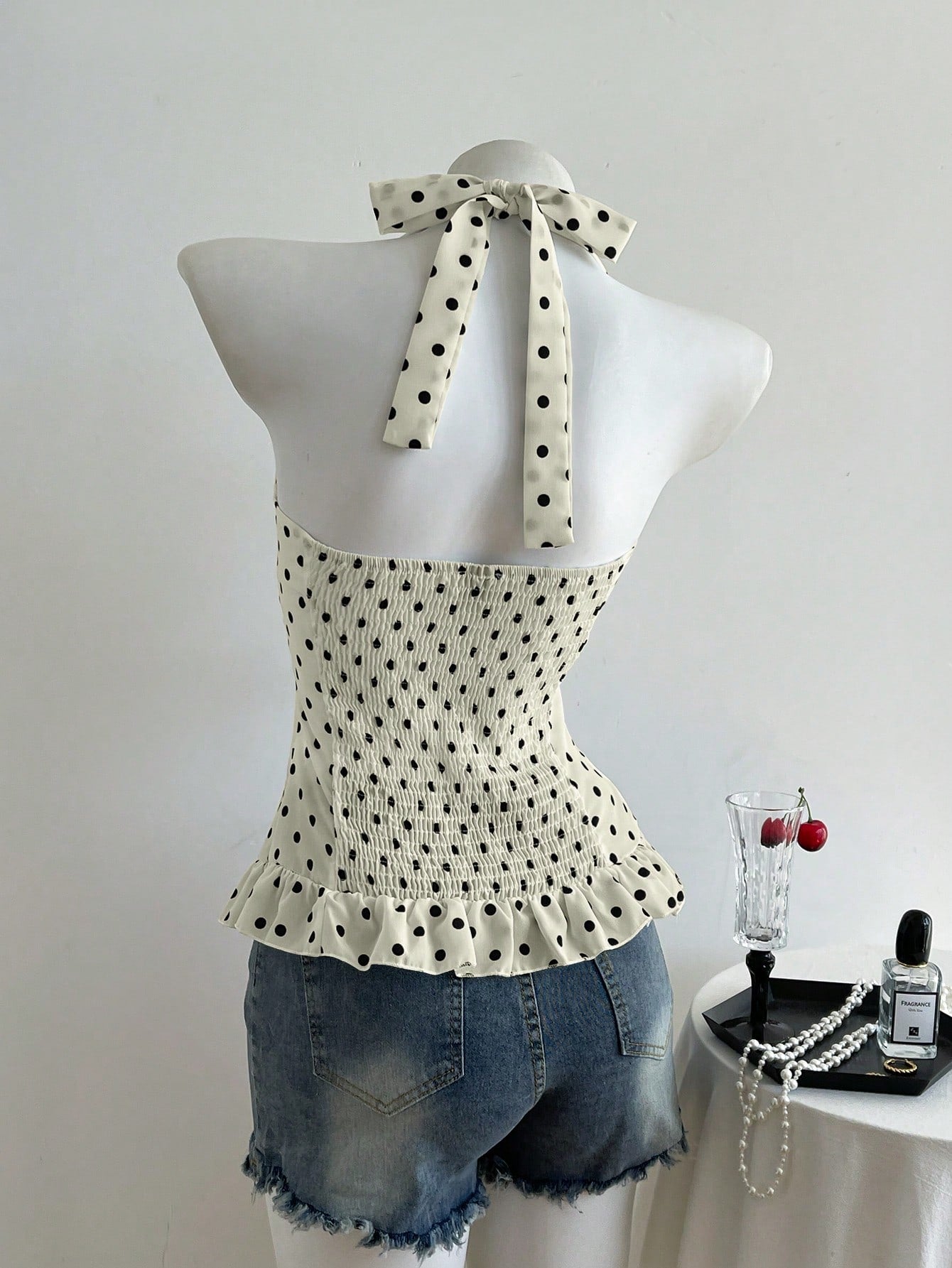 Women's polka dot halter camisole with bow bust detail, ruched and shirred design, slim crop fit, and flared ruffle hem.