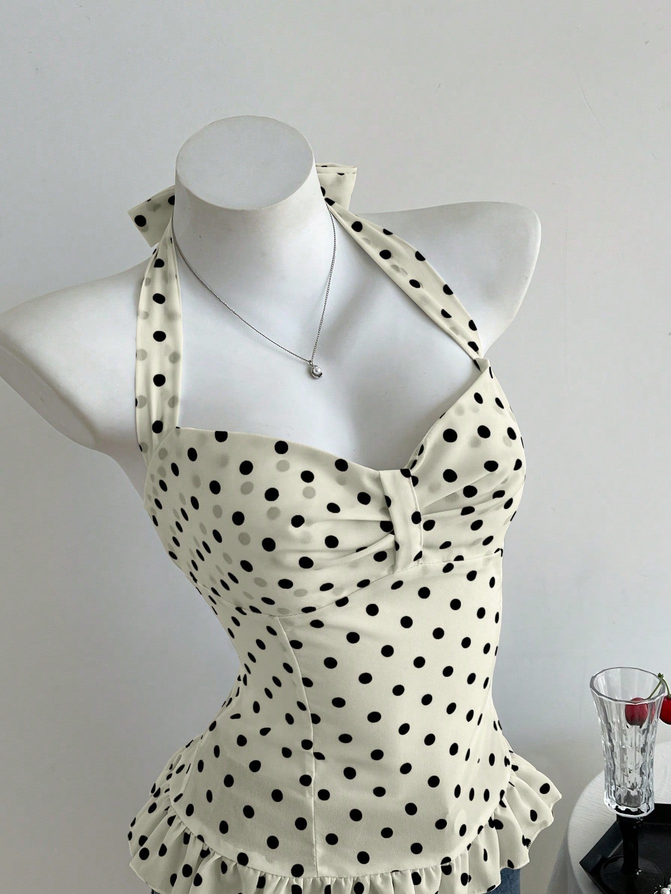 Women's polka dot halter camisole with bow bust detail, ruched and shirred design, slim crop fit, and flared ruffle hem.