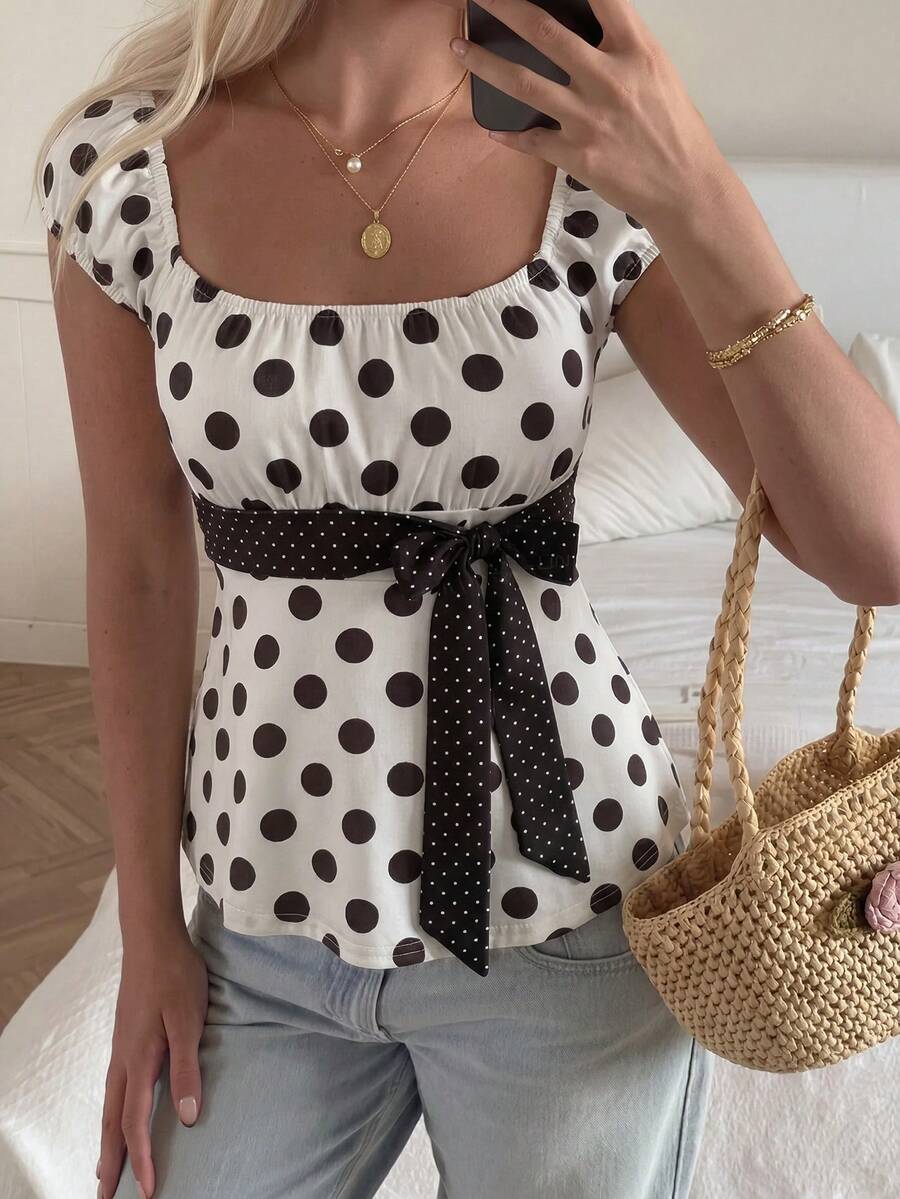Women's short sleeve square neck polka dot top with ruched detailing, flared hem, and waist tie back.