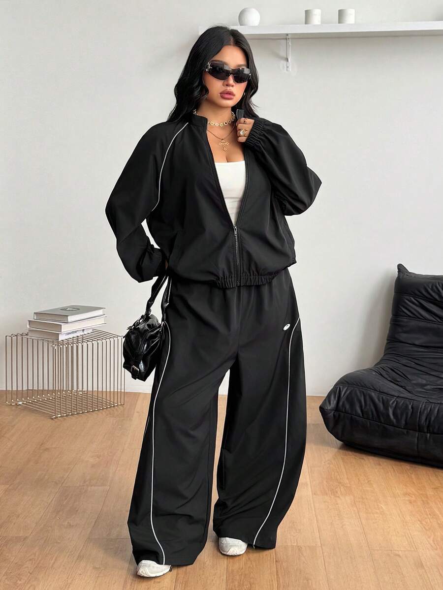 Women's plus size two-piece casual tracksuit set in black, featuring a loose-fit zip-up jacket with stand collar and matching cropped parachute pants.