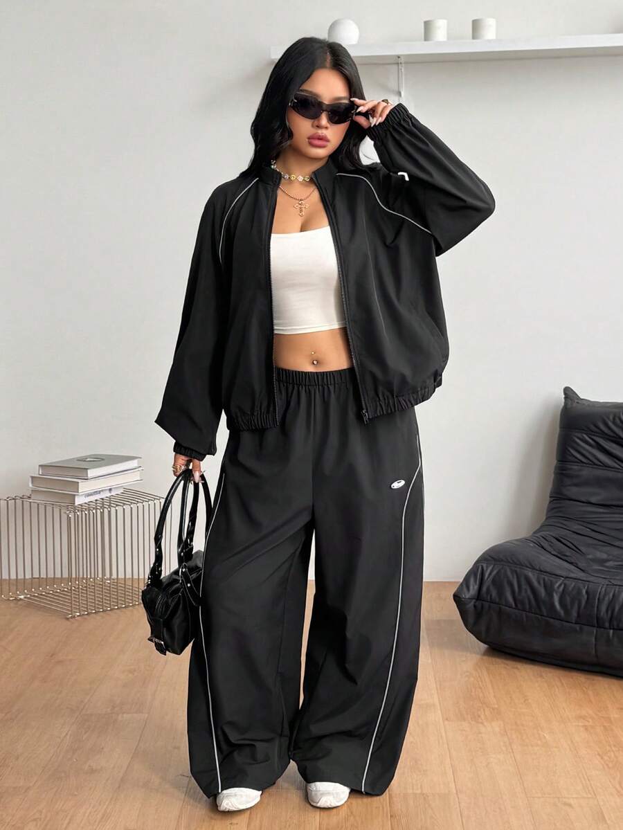 Women's plus size two-piece casual tracksuit set in black, featuring a loose-fit zip-up jacket with stand collar and matching cropped parachute pants.