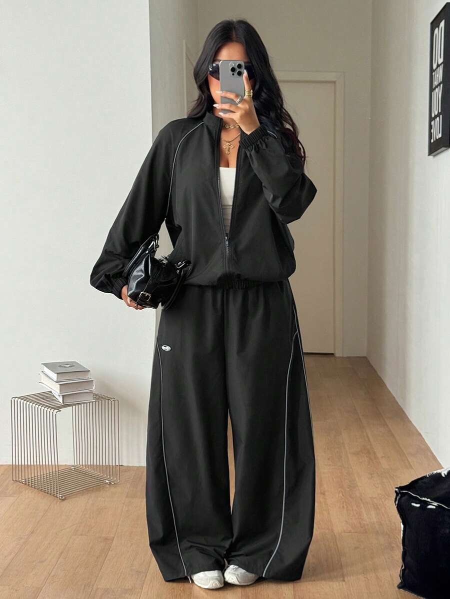 Women's plus size two-piece casual tracksuit set in black, featuring a loose-fit zip-up jacket with stand collar and matching cropped parachute pants.