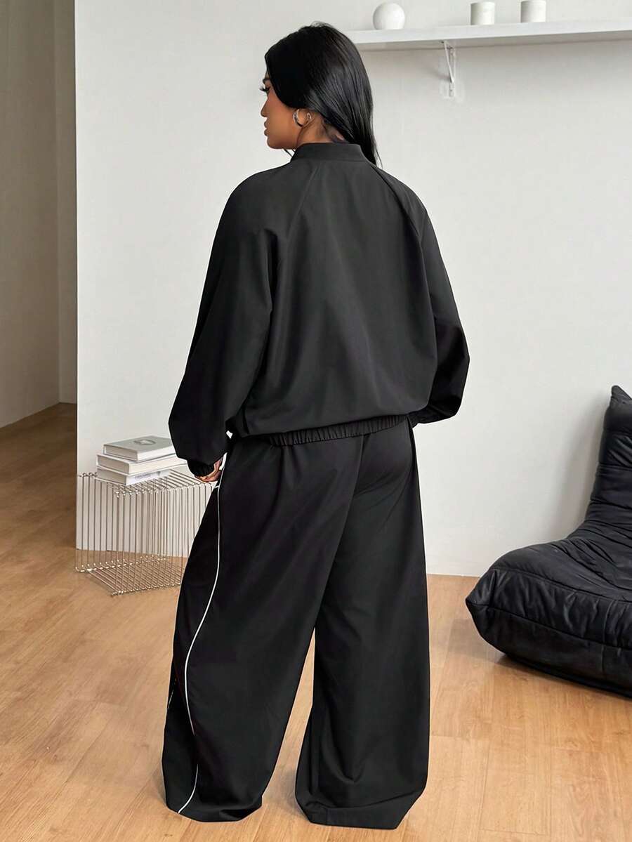 Women's plus size two-piece casual tracksuit set in black, featuring a loose-fit zip-up jacket with stand collar and matching cropped parachute pants.