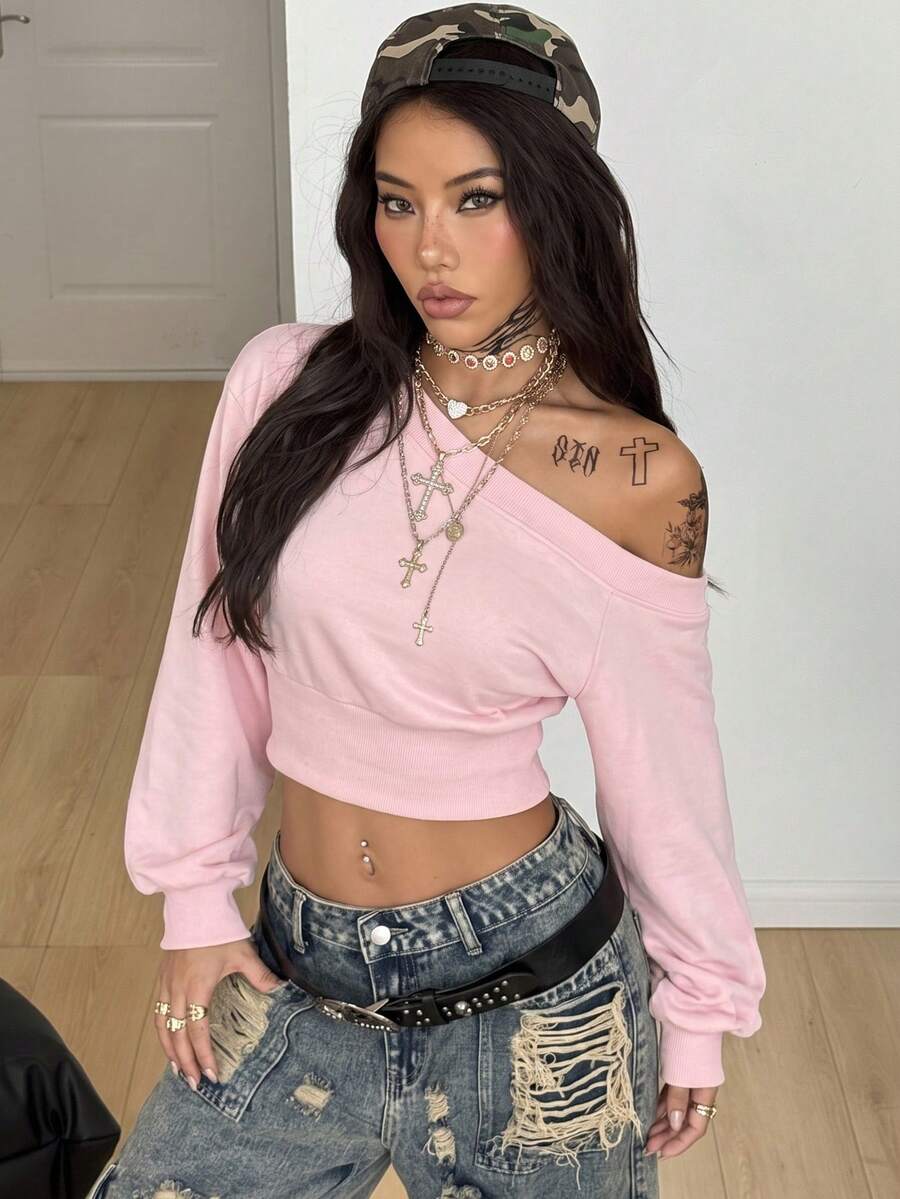 Baby pink off shoulder sweatshirt with asymmetrical neckline and long drop shoulder sleeves on a female model.