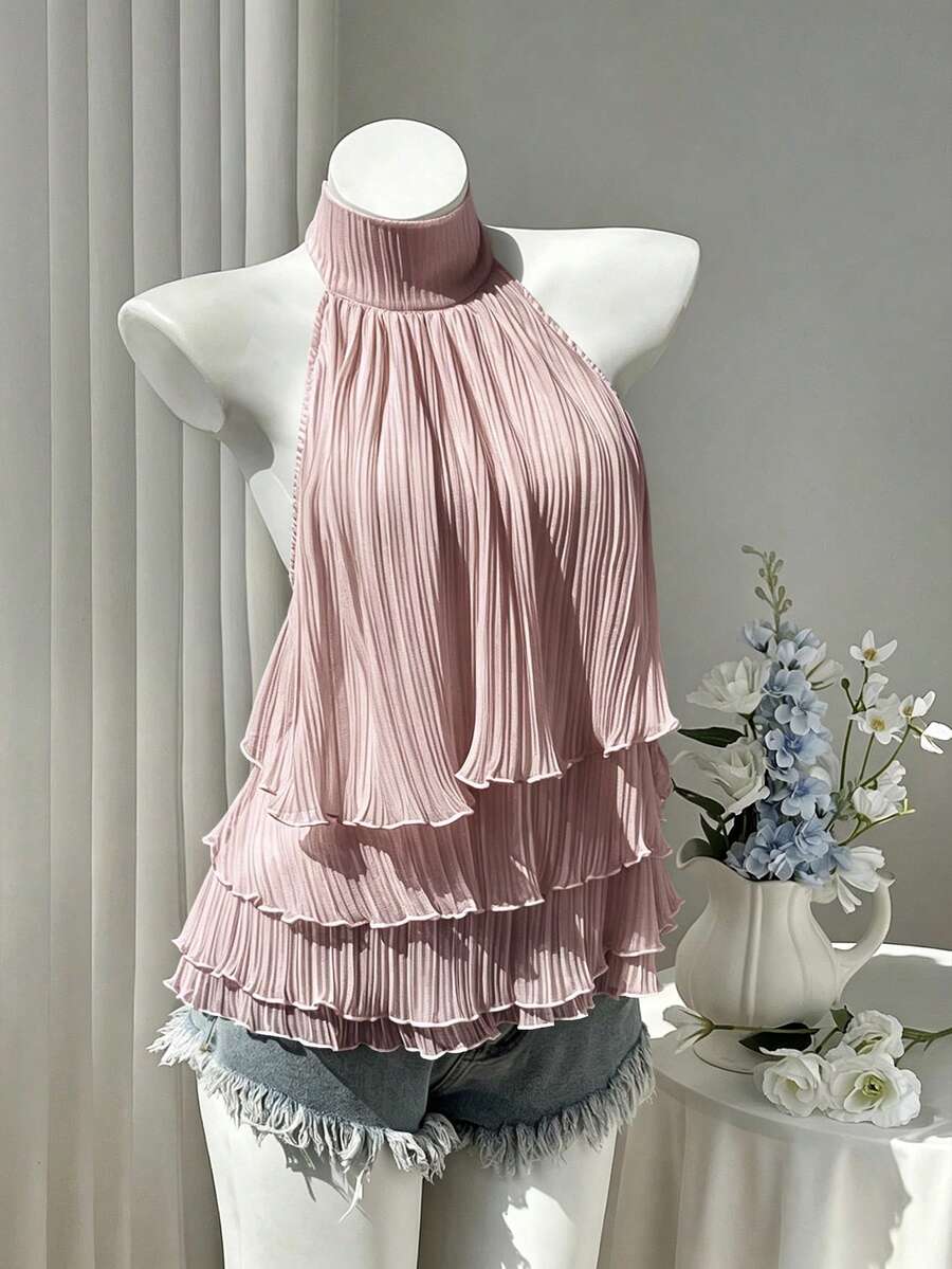 Women's white sleeveless halter neck top featuring pleated fabric, backless tie strap design, and a flared layered ruffle hem.