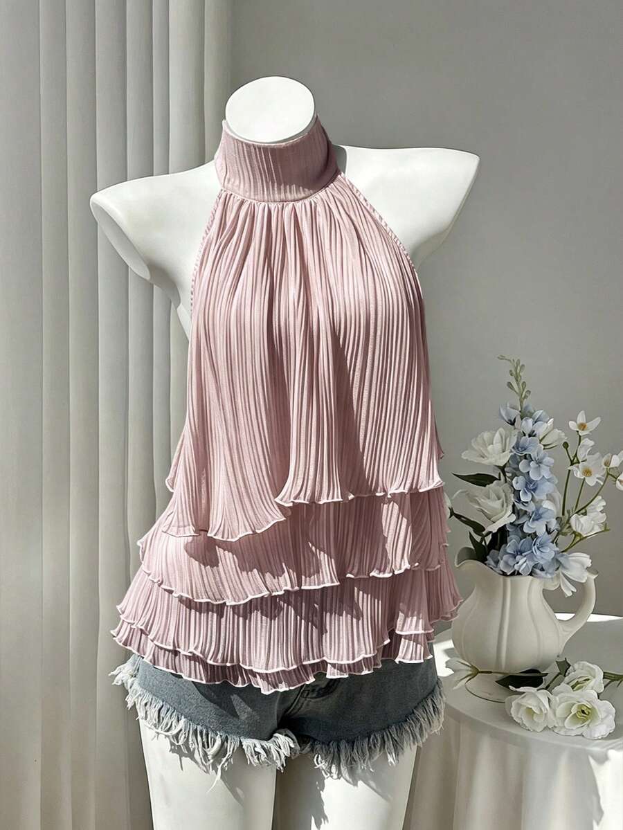 Women's white sleeveless halter neck top featuring pleated fabric, backless tie strap design, and a flared layered ruffle hem.