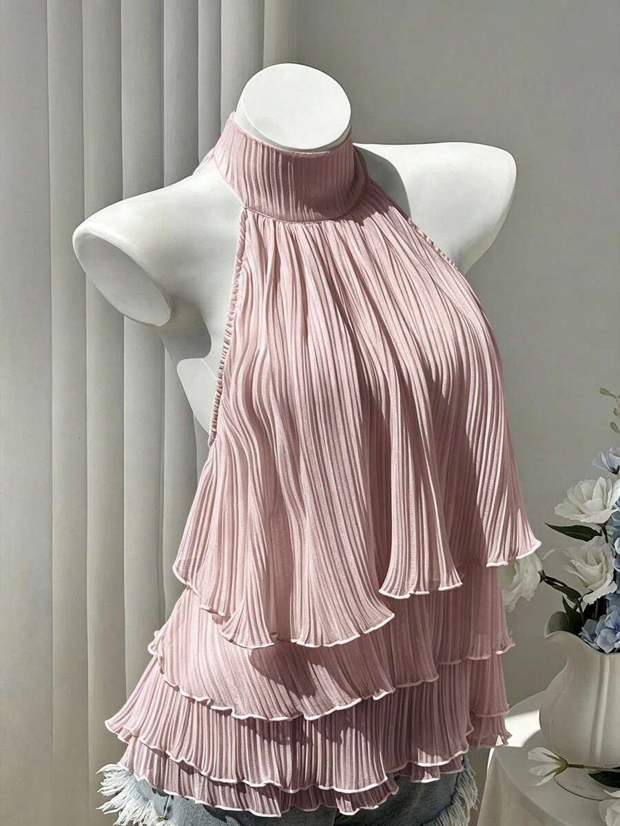 Women's white sleeveless halter neck top featuring pleated fabric, backless tie strap design, and a flared layered ruffle hem.