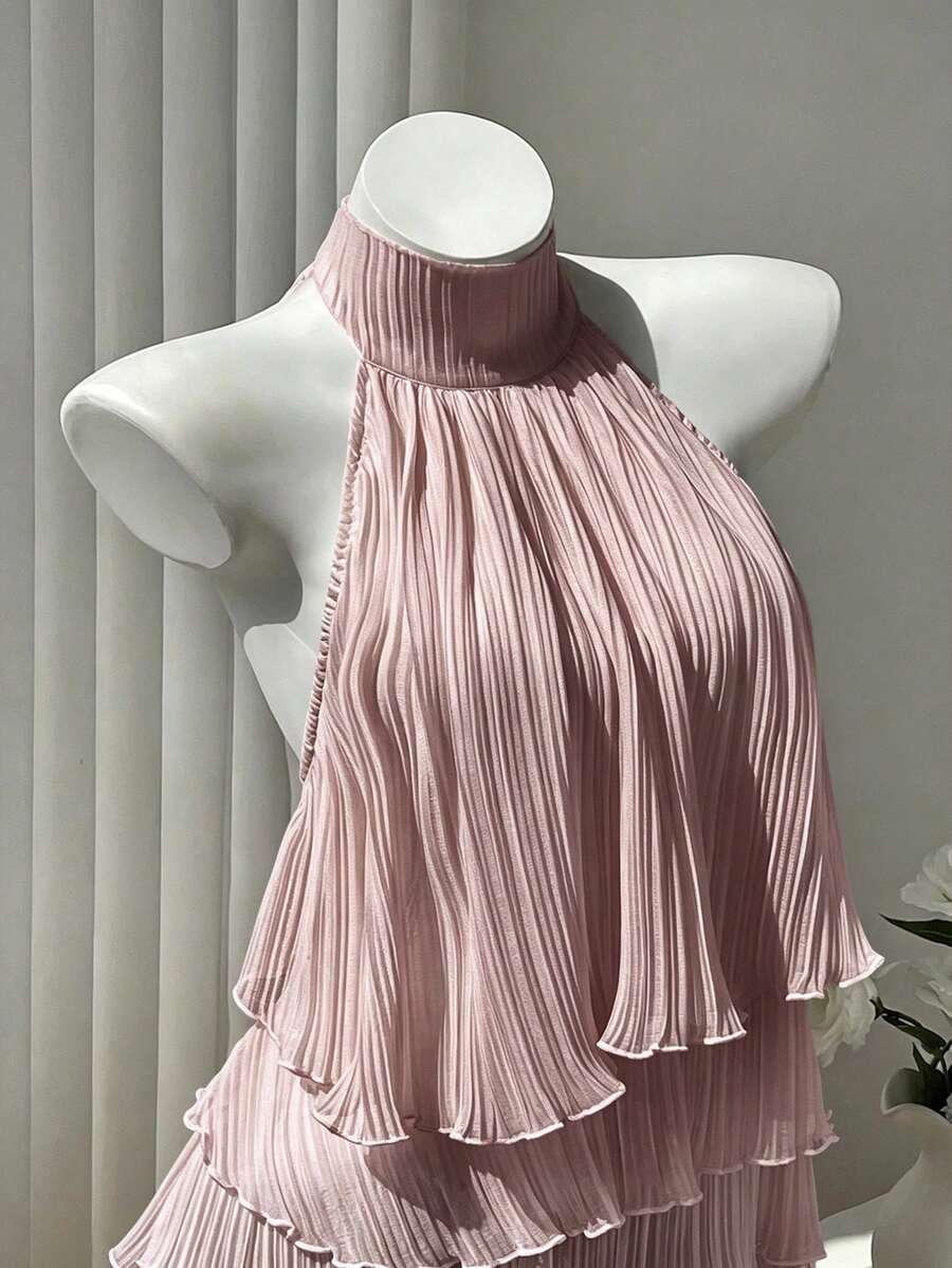 Women's white sleeveless halter neck top featuring pleated fabric, backless tie strap design, and a flared layered ruffle hem.