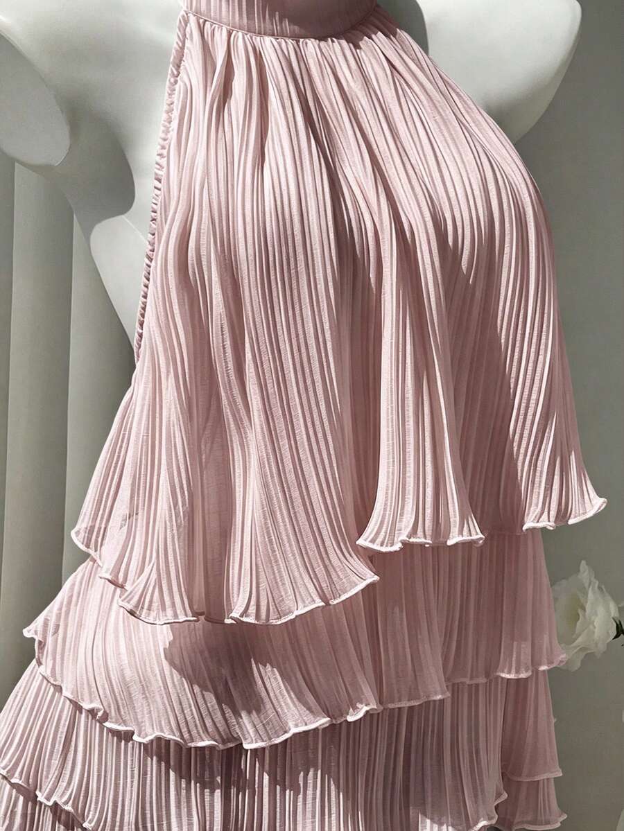 Women's white sleeveless halter neck top featuring pleated fabric, backless tie strap design, and a flared layered ruffle hem.