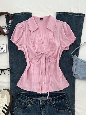 Pink short sleeve V-neck blouse featuring flounce sleeves, lace-up bow tie detail, ruffle accents, and button front closures.