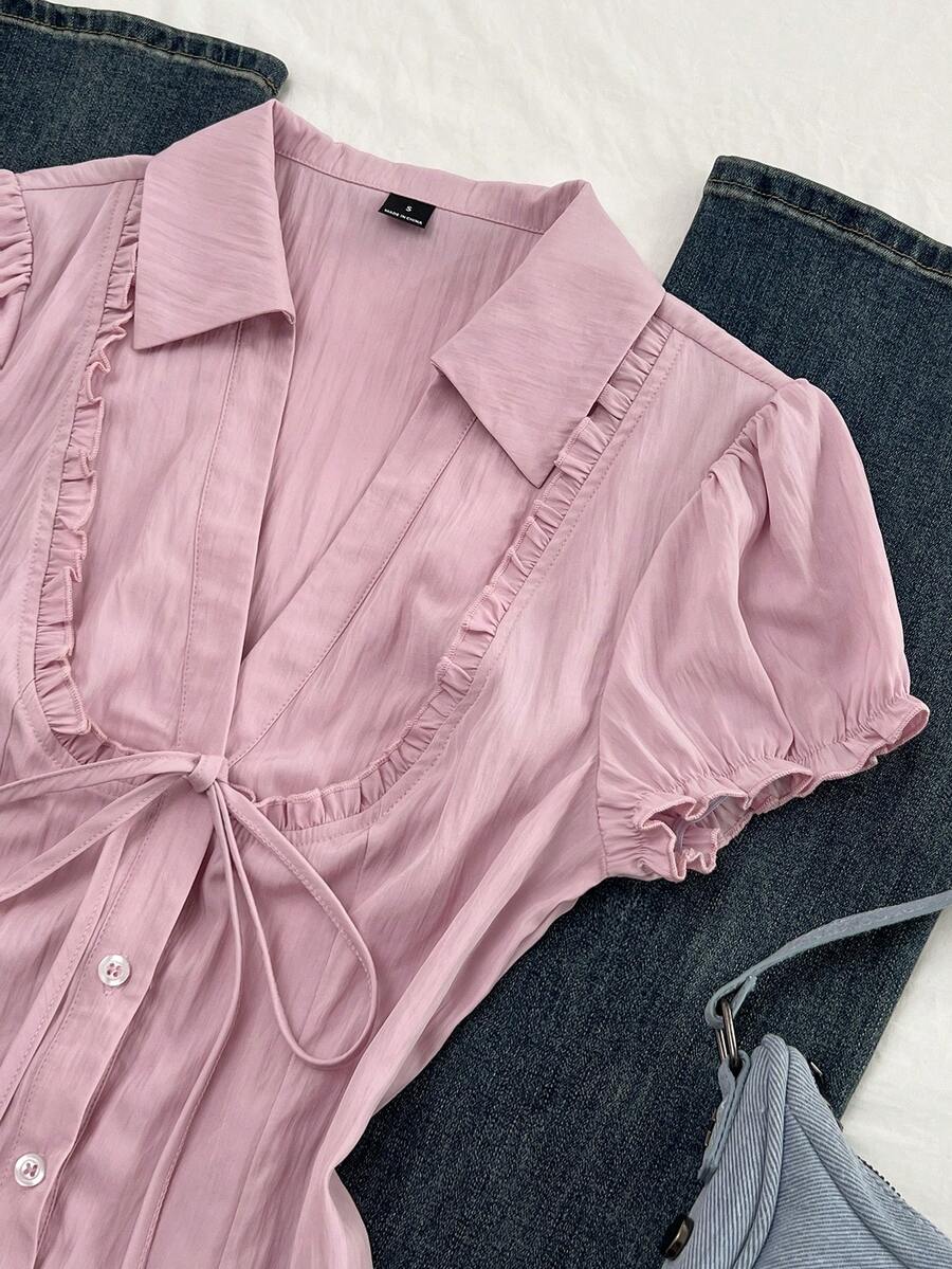 Pink short sleeve V-neck blouse featuring flounce sleeves, lace-up bow tie detail, ruffle accents, and button front closures.