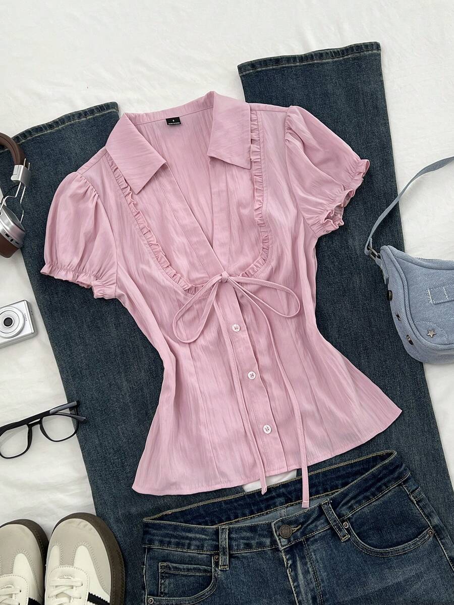 Pink short sleeve V-neck blouse featuring flounce sleeves, lace-up bow tie detail, ruffle accents, and button front closures.