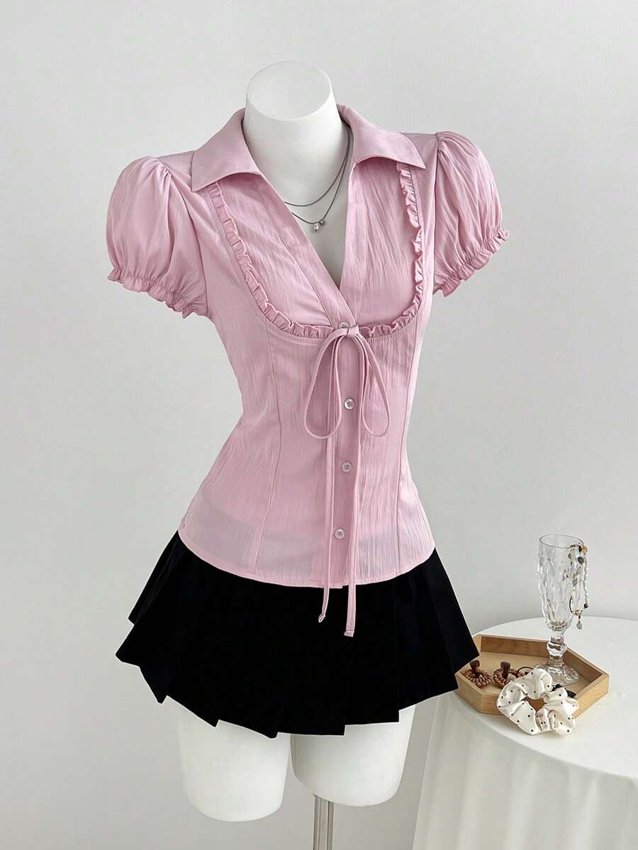 Pink short sleeve V-neck blouse featuring flounce sleeves, lace-up bow tie detail, ruffle accents, and button front closures.