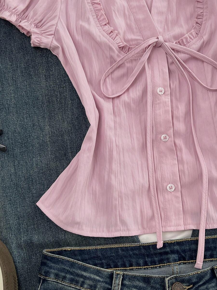 Pink short sleeve V-neck blouse featuring flounce sleeves, lace-up bow tie detail, ruffle accents, and button front closures.