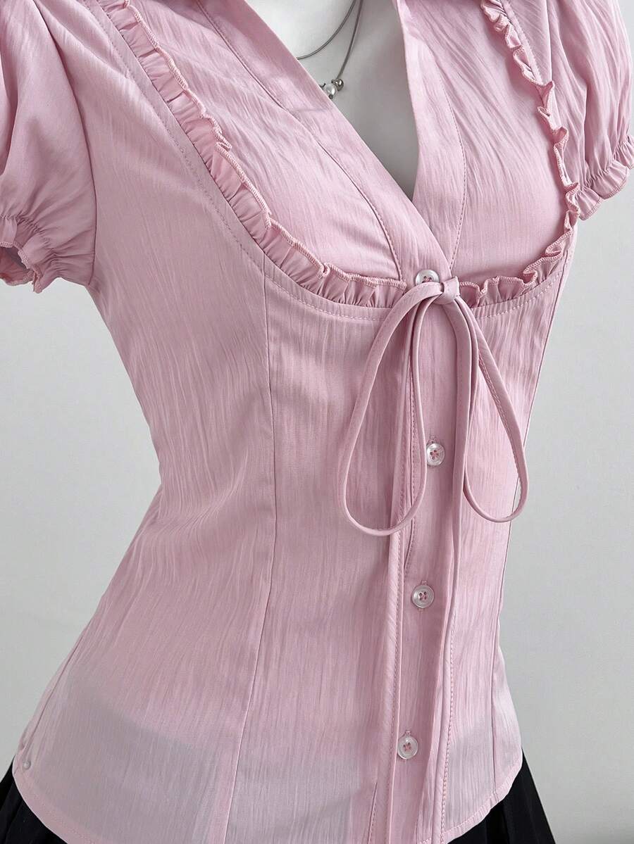 Pink short sleeve V-neck blouse featuring flounce sleeves, lace-up bow tie detail, ruffle accents, and button front closures.