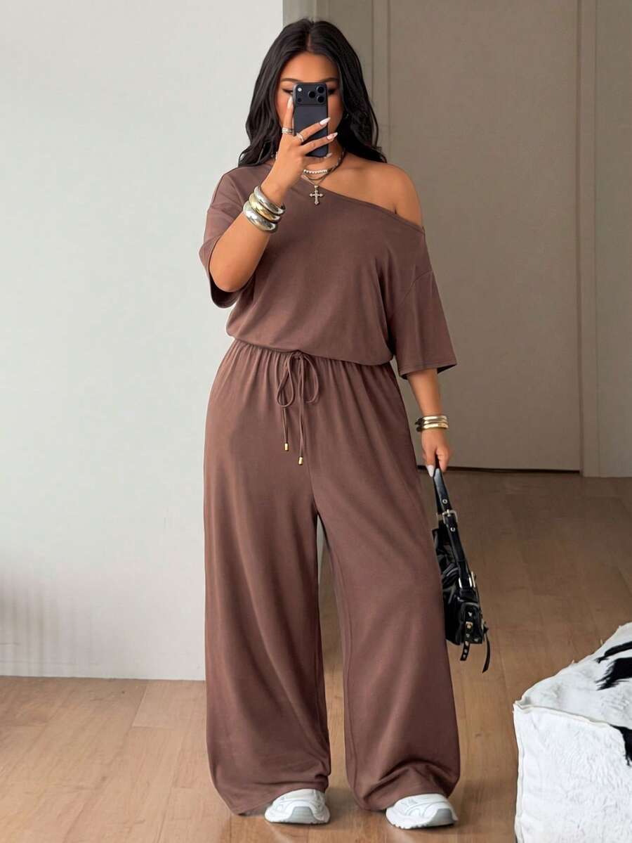Plus size women's wide leg jumpsuit in dark grey featuring an asymmetrical neckline, short batwing sleeves, and a drawstring high waist with side pockets.