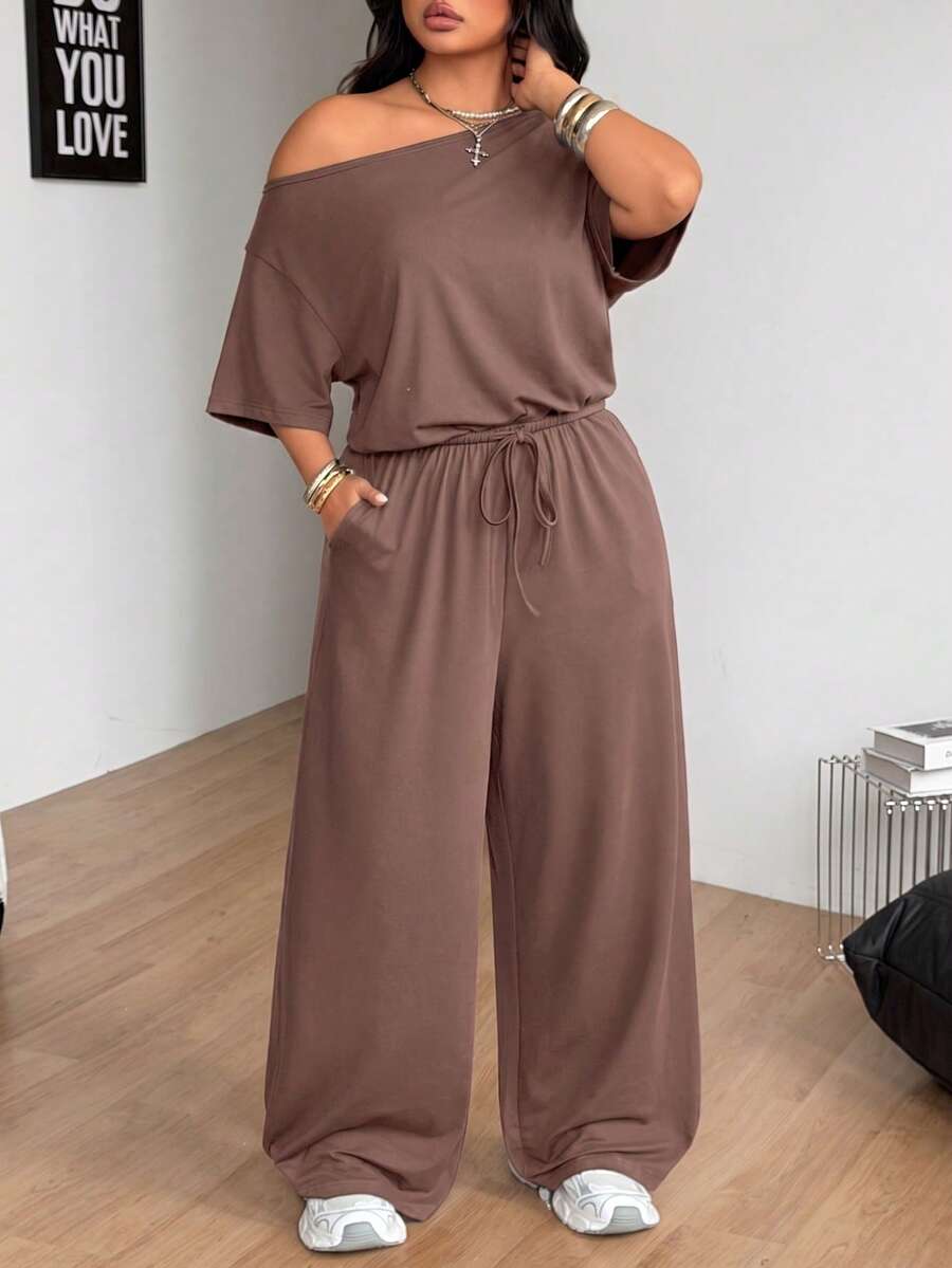 Plus size women's wide leg jumpsuit in dark grey featuring an asymmetrical neckline, short batwing sleeves, and a drawstring high waist with side pockets.
