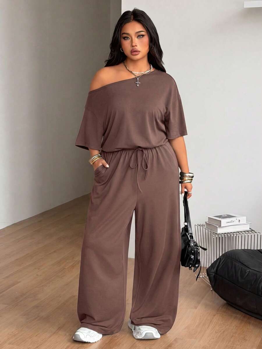 Plus size women's wide leg jumpsuit in dark grey featuring an asymmetrical neckline, short batwing sleeves, and a drawstring high waist with side pockets.