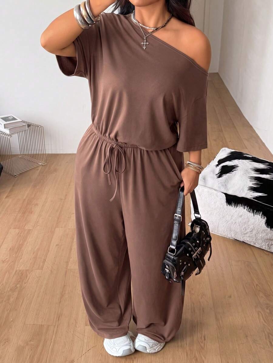 Plus size women's wide leg jumpsuit in dark grey featuring an asymmetrical neckline, short batwing sleeves, and a drawstring high waist with side pockets.