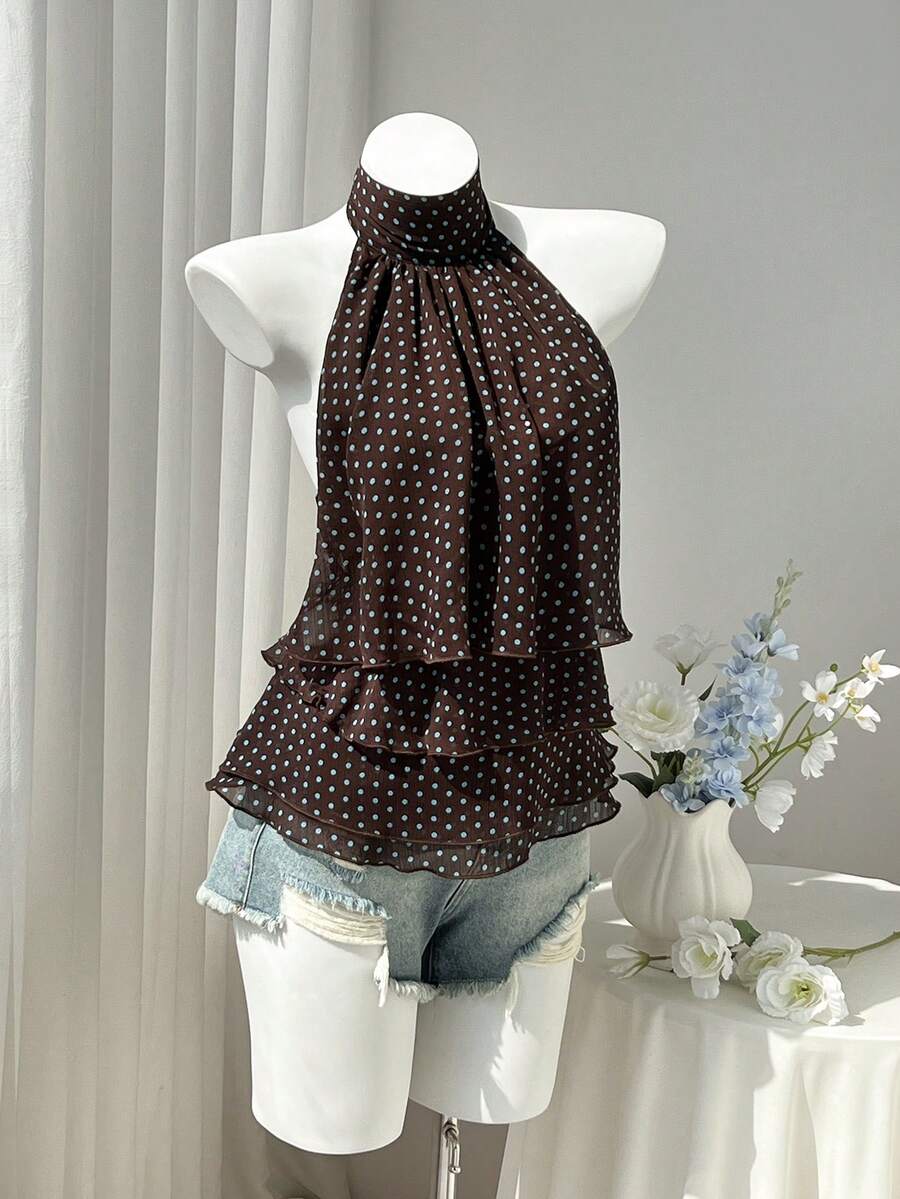 Women's white sleeveless halter neck top featuring pleated fabric, backless tie strap design, and a flared layered ruffle hem.