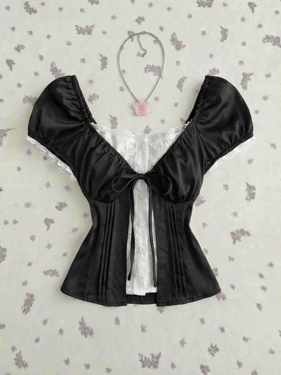 Women's black 2-in-1 blouse featuring a sweetheart neckline, short puff sleeves, front tie bow accent, and asymmetrical hem.