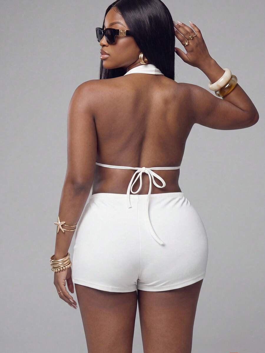 Front and back view of a women's white backless halter romper featuring a draped cowl neckline and fitted short unitard design.