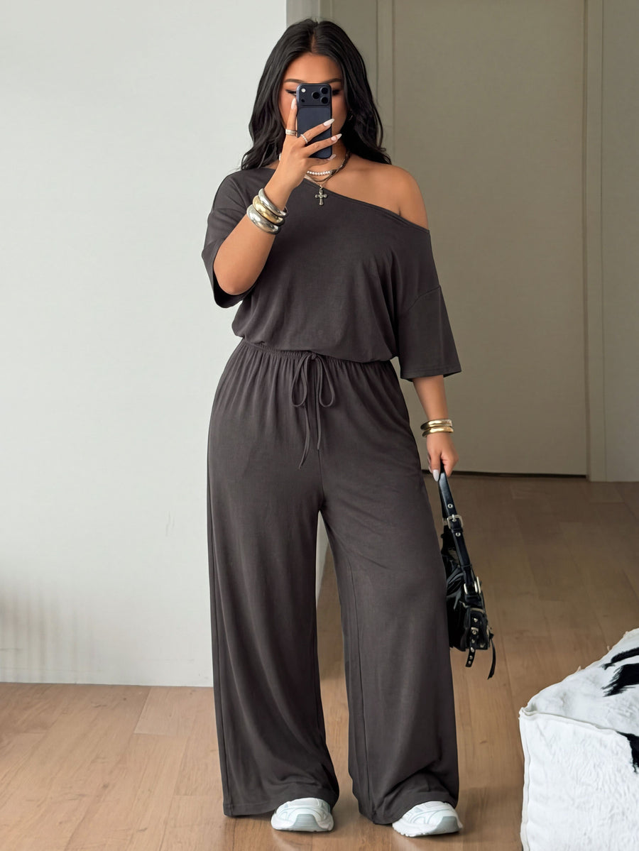 Plus size women's wide leg jumpsuit in dark grey featuring an asymmetrical neckline, short batwing sleeves, and a drawstring high waist with side pockets.