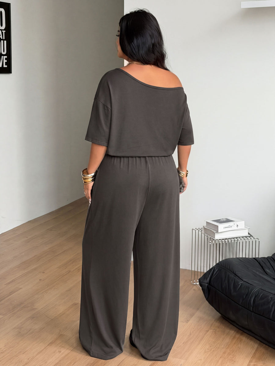 Plus size women's wide leg jumpsuit in dark grey featuring an asymmetrical neckline, short batwing sleeves, and a drawstring high waist with side pockets.
