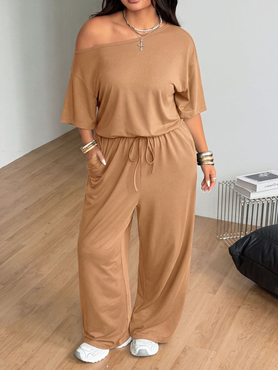 Plus size women's wide leg jumpsuit in dark grey featuring an asymmetrical neckline, short batwing sleeves, and a drawstring high waist with side pockets.