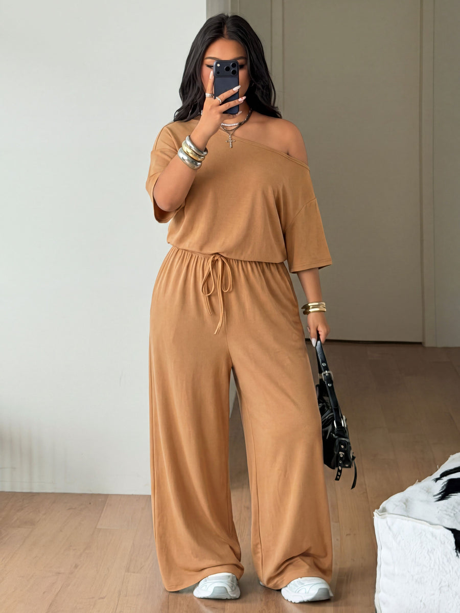 Plus size women's wide leg jumpsuit in dark grey featuring an asymmetrical neckline, short batwing sleeves, and a drawstring high waist with side pockets.