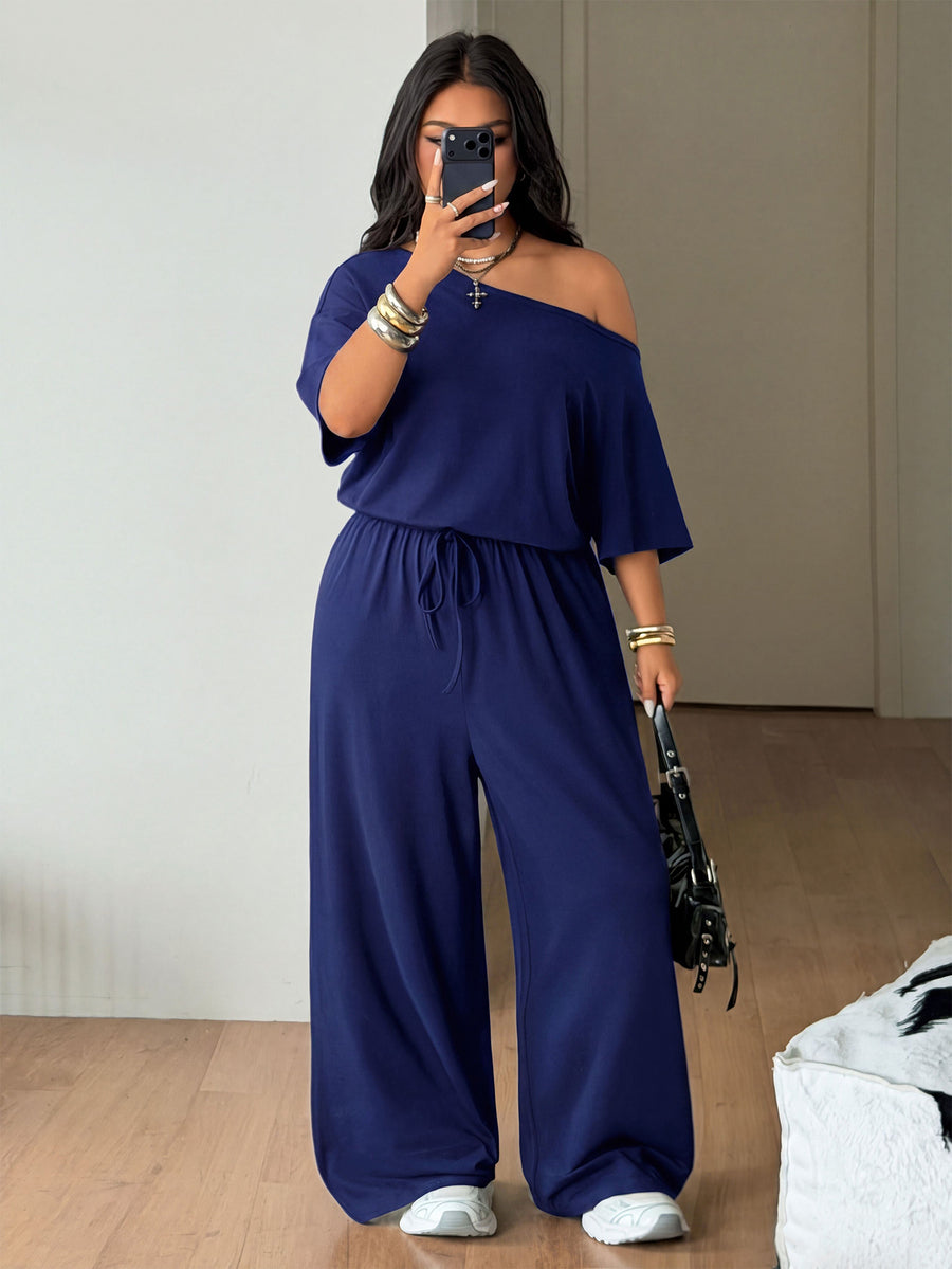 Plus size women's wide leg jumpsuit in dark grey featuring an asymmetrical neckline, short batwing sleeves, and a drawstring high waist with side pockets.