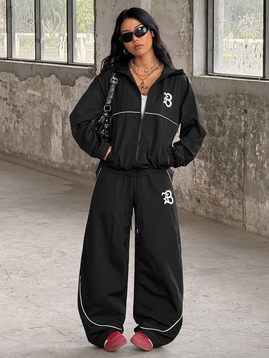 Two-piece black streetwear tracksuit set featuring a hooded windbreaker jacket with contrast piping and matching long jogger pants.