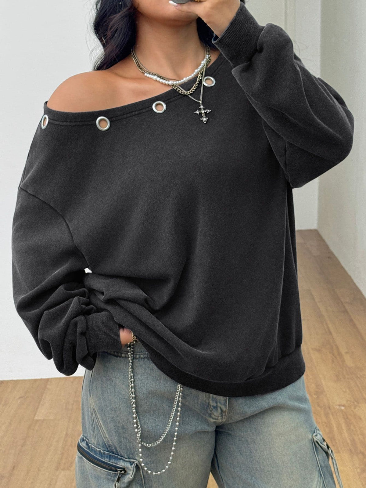 Women's oversized dark grey long sleeve sweatshirt featuring an asymmetrical boat neckline with grommet eyelet details and drop shoulders.