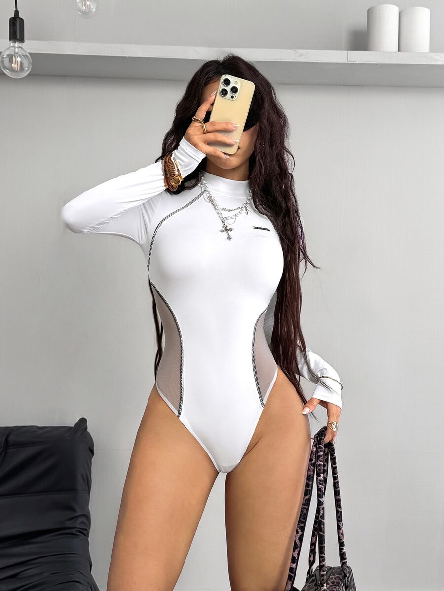 White long sleeve knit bodysuit featuring a front zip-up stand collar and contrast sheer mesh panels in a slim fit silhouette.