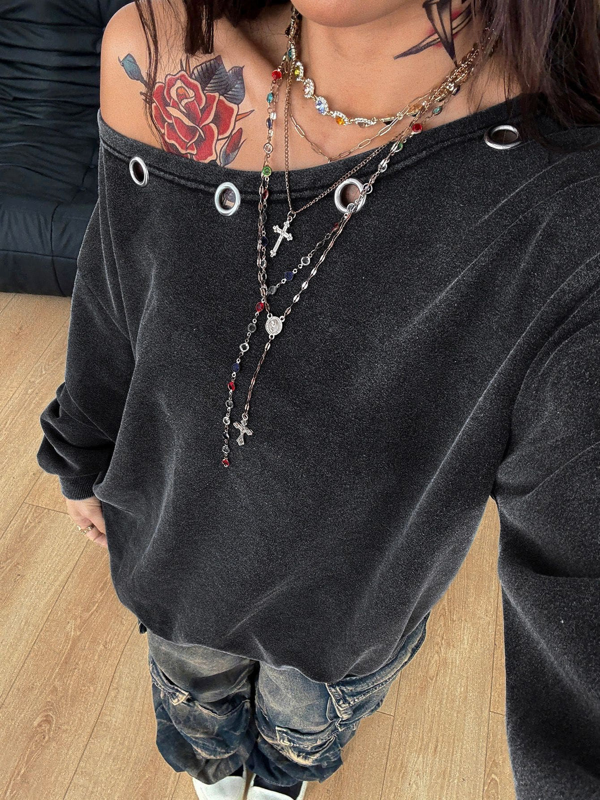 Women's oversized dark grey long sleeve sweatshirt featuring an asymmetrical boat neckline with grommet eyelet details and drop shoulders.