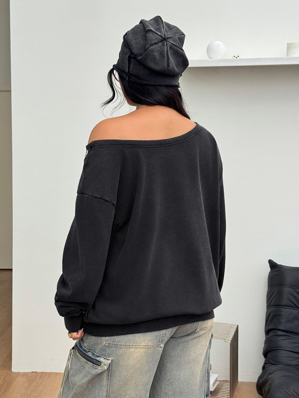Women's oversized dark grey long sleeve sweatshirt featuring an asymmetrical boat neckline with grommet eyelet details and drop shoulders.